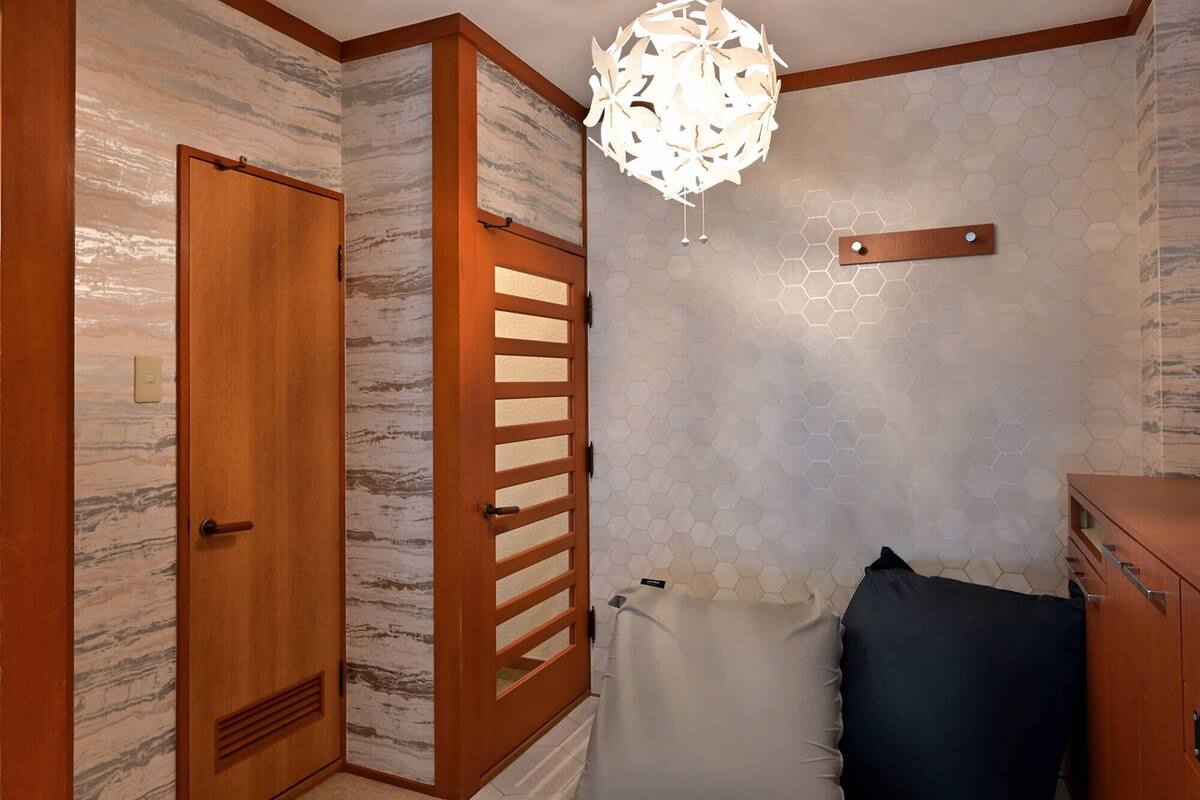 Een gang met een houten deur, een wand met een honingraatpatroon en een hanglamp.