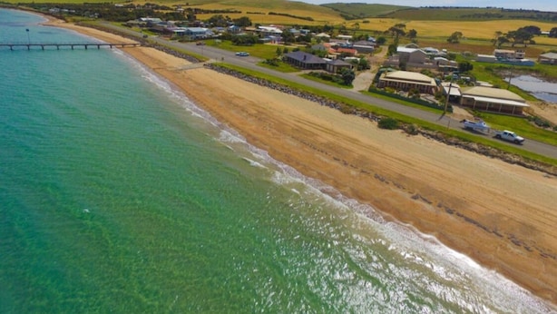 Vista aérea de una zona costera con playa, muelle y un conjunto de edificios.