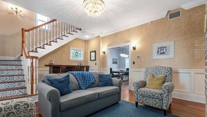 Ein geräumiges Wohnzimmer mit grauem Sofa, einem gemusterten Sessel und einer Treppe zu einer weiteren Ebene.