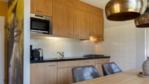 Een moderne keuken met houten kastjes, een roestvrijstalen magnetron, een gasfornuis en een zwarte koffiezetapparaat.