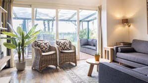 Een gezellige woonkamer met rieten stoelen, een grijze bank en een potplant.
