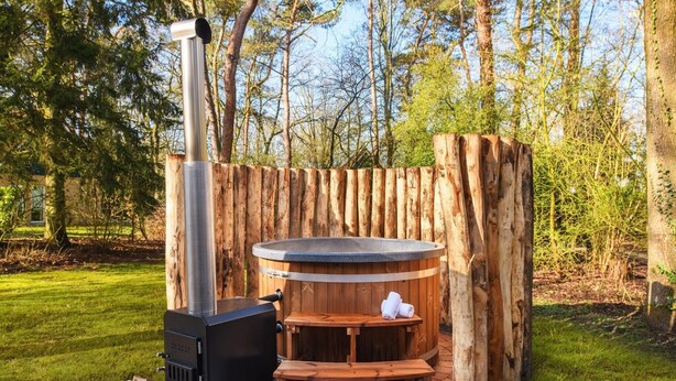 Een houtkachel met schoorsteen, een houten bank en een hottub in een rustieke buitenomgeving.