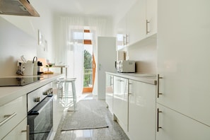 A modern kitchen with white cabinets, a built-in oven, and a dining area with a table and chairs.