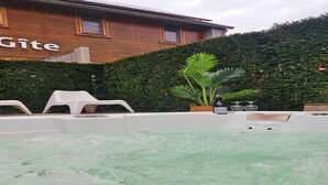 A hot tub with a wooden wall and a hedge in the background.