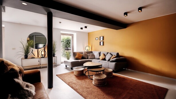 A modern living room with a sofa, coffee table, and ottomans. There is a large window with a view of greenery outside.