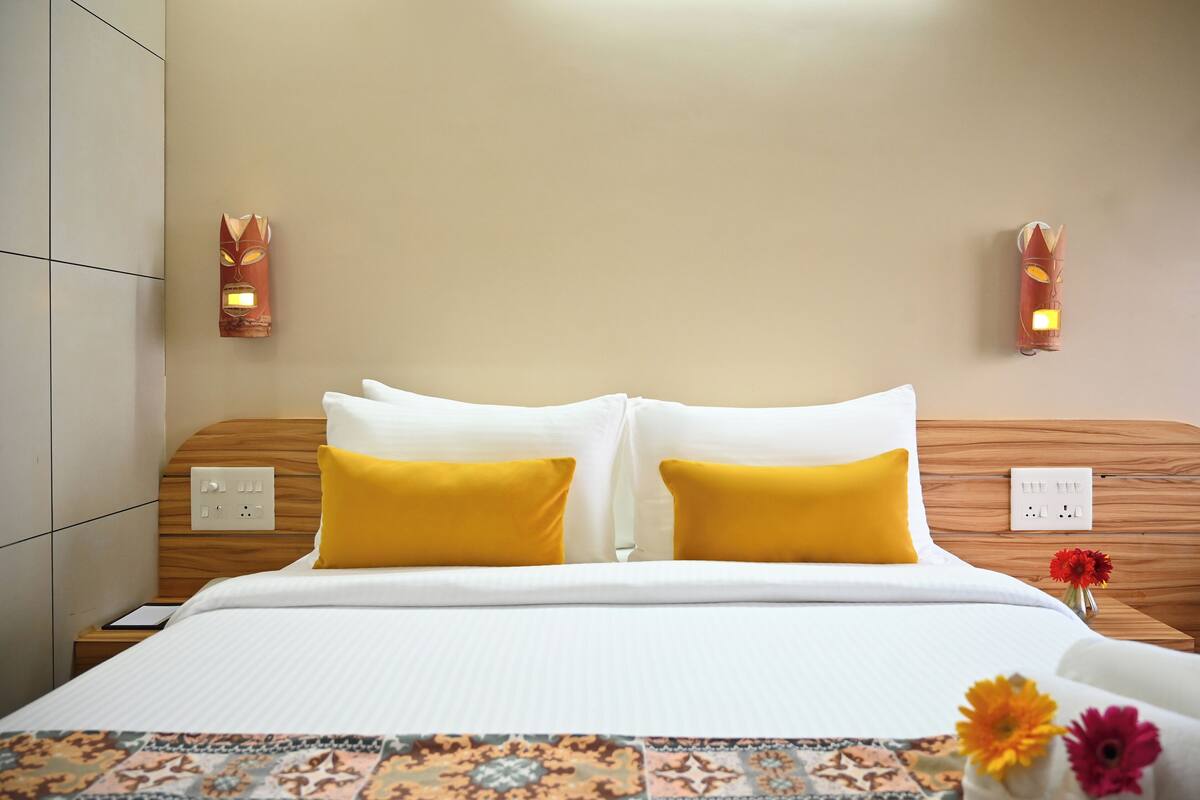 Ein Hotelzimmer mit einem ordentlich bezogenen Bett, zwei Wandleuchten, einem Nachttisch mit Steckdose und einer zudeckenden Bettdecke mit Blumenmuster.