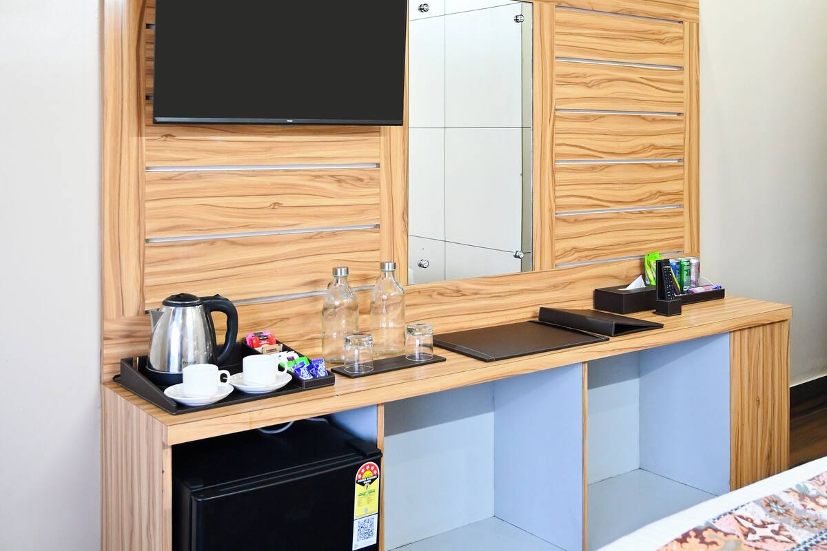 Ein kleines Hotelzimmer mit Küchenzeile, einem Flachbildfernseher an einer Holzwand, einem kleinen Kühlschrank und einem Bett mit einem gemusterten Bettbezug.