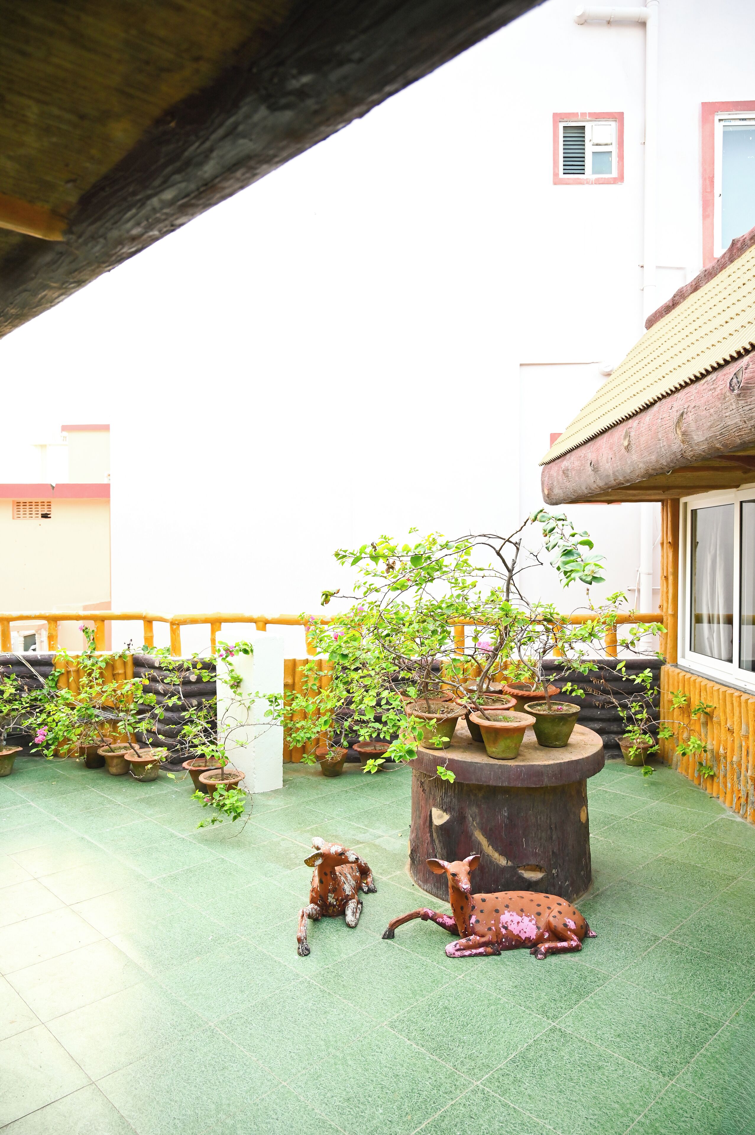 A rooftop garden with potted plants, a decorative deer sculpture, and a wooden table.