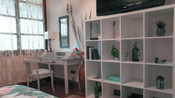 A bedroom with a desk, chair, TV, and shelves with various items.