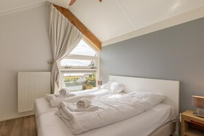 A bedroom with a large bed, a window with curtains, a bedside table with a lamp, and a radiator.