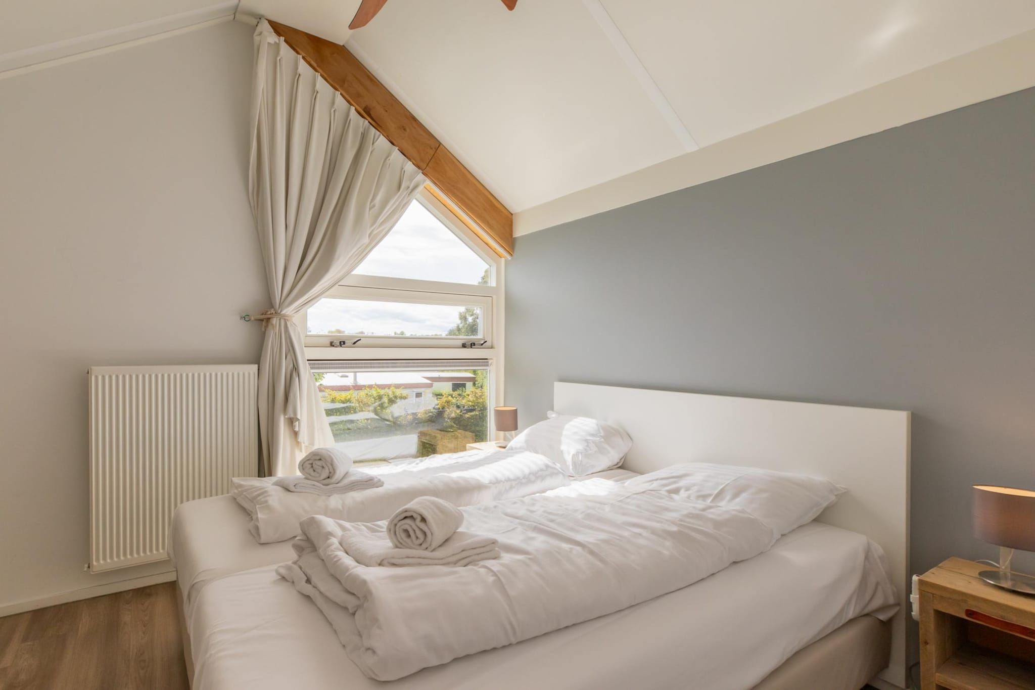 A bedroom with a large bed, a window with curtains, a radiator, and a bedside table with a lamp.