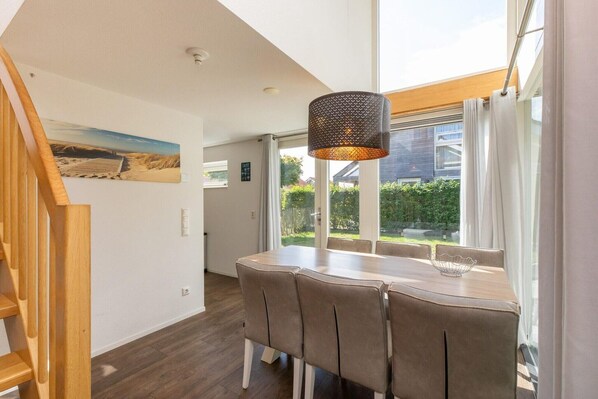 Un espace repas comprenant une table et des chaises, une lampe suspendue et une vue sur l ’extérieur grâce à de grandes fenêtres.