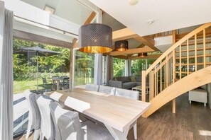 Un interior moderno con comedor, una escalera y ventanas amplias.