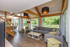 Un vaste espace de vie doté d’un plancher en bois, d’un canapé gris, d’une table basse et d’un escalier menant à un autre niveau.
