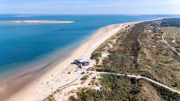 An aerial view of a beach with a sandy shore, a small building, and a road winding through the landscape. - Modern Chalet near Beach in Renesse (Renesse)