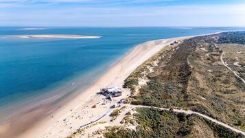 Luchtbeeld van een strand met een complex van gebouwen, waaronder een groot gebouw met een schuin dak, gelegen aan de zandkust.
