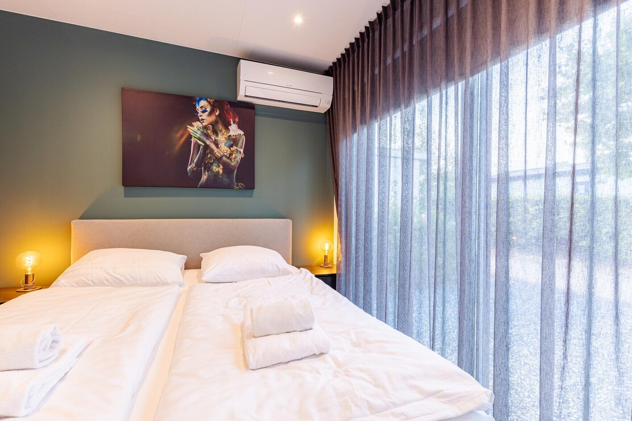 Een hotelkamer met een bed, twee bedlampen, een schilderij aan de muur en een raam met gordijnen.