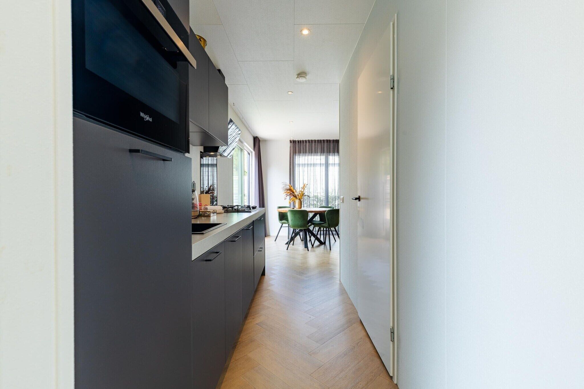 Eine moderne Küche mit Einbauherd, ein Essbereich mit Tisch und Stühlen sowie ein Blick auf den Essbereich durch ein Fenster.