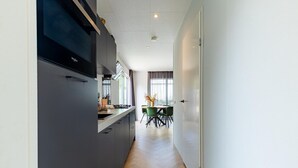 A modern kitchen with a built-in stove, a dining area with a table and chairs, and a view of the dining area through a window. - Modern Chalet near Beach in Renesse (Renesse)