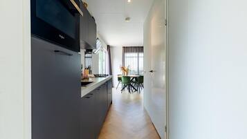 Eine moderne Küche mit Einbauherd, ein Essbereich mit Tisch und Stühlen sowie ein Blick auf den Essbereich durch ein Fenster.