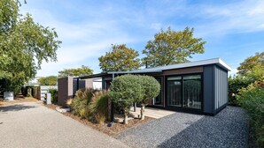A modern house with a gravel driveway, a small garden with shrubs and a tree, and a clear blue sky. - Modern Chalet near Beach in Renesse (Renesse)