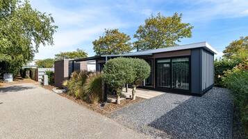 Ein modernes Haus mit Kiesauffahrt, ein kleiner Garten mit Sträuchern und einem Baum, und einem strahlend blauen Himmel.