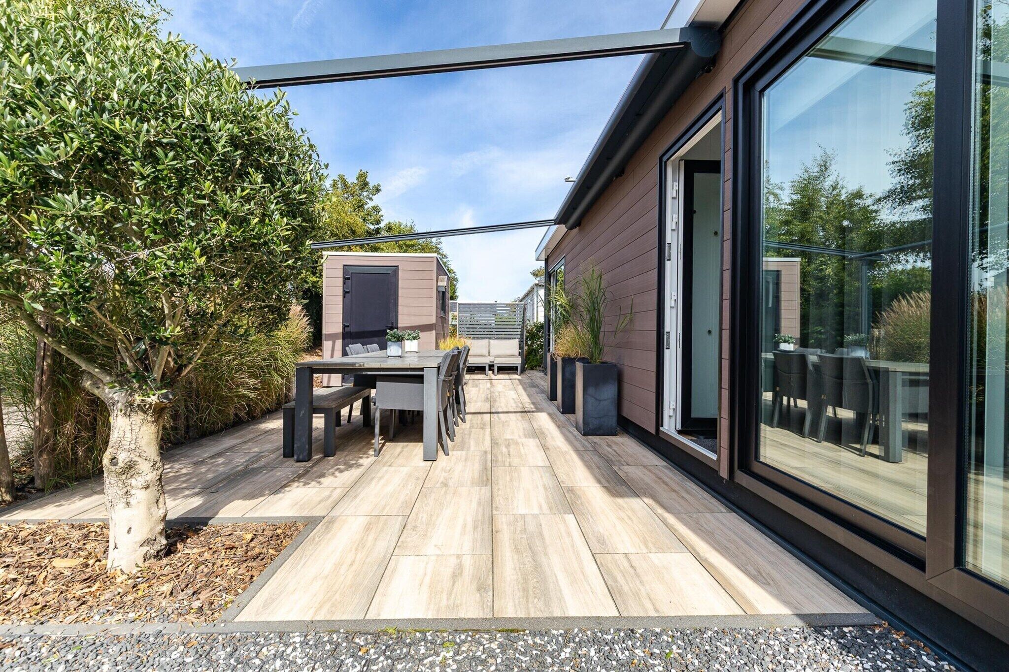 Een modern buitenterras met een eettafel en stoelen, omgeven door een houten terras en een glazen constructie.
