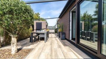 Eine moderne Außenpatio mit Esstisch und Stühlen, umgeben von einer Holzterrasse und einer Glaseinfassung.