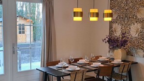Un comedor con una mesa lista para cuatro personas, un jarrón con flores moradas y una pared con estampado floral.