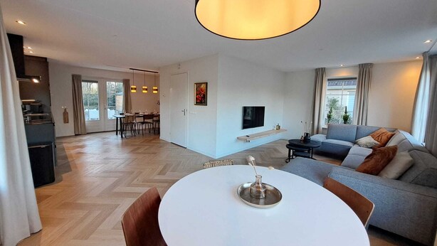 Una sala de estar moderna con una mesa redonda blanca, un sofá gris y un televisor en la pared.