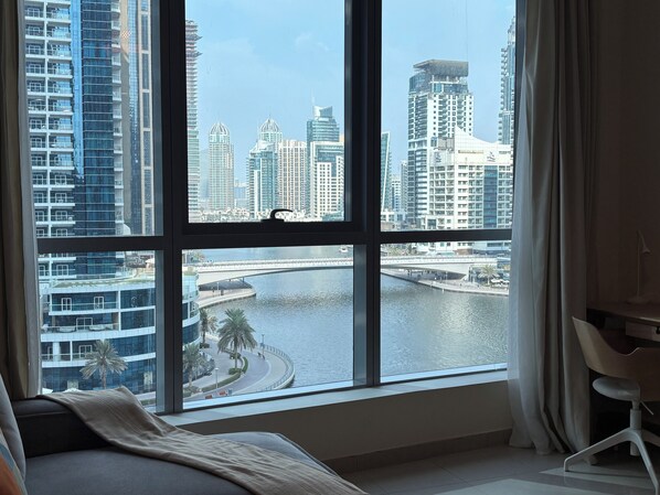 A modern hotel room with a large window offering a view of a city skyline and a river.