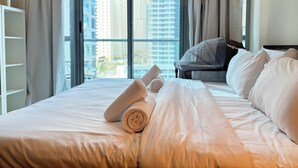 A hotel room with a bed, pillows, a chair, and a view of tall buildings through the window.