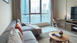 A modern living room with a sofa, a coffee table, a TV, and a large window offering a city view.