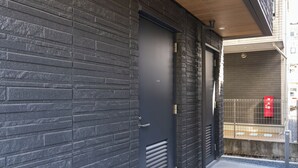 Un bâtiment moderne avec une façade en briques sombres, une porte en métal et une petite fenêtre ornée d’une boîte aux lettres rouge.