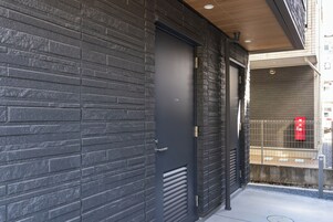 Fachada moderna de ladrillo oscuro, puerta metálica y un ventanal con buzón rojo.
