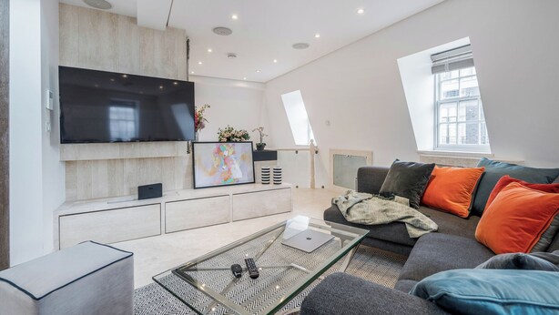 Una sala de estar moderna con un televisor de pantalla plana, un sofá con cojines coloridos, una mesa de centro y un ventanal que proporciona luz natural.