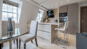 Una cocina moderna con una mesa de comedor de vidrio, taburetes de bar y un televisor integrado.