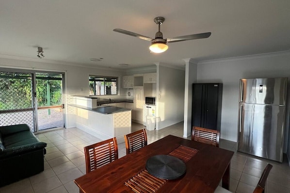A modern kitchen with a central island, a dining area with a wooden table and chairs, a refrigerator, and a ceiling fan.