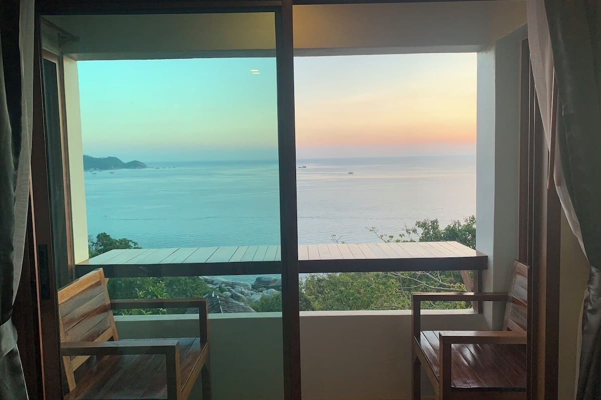 A room with a large window overlooking a body of water and distant land. There are two wooden benches in the room.