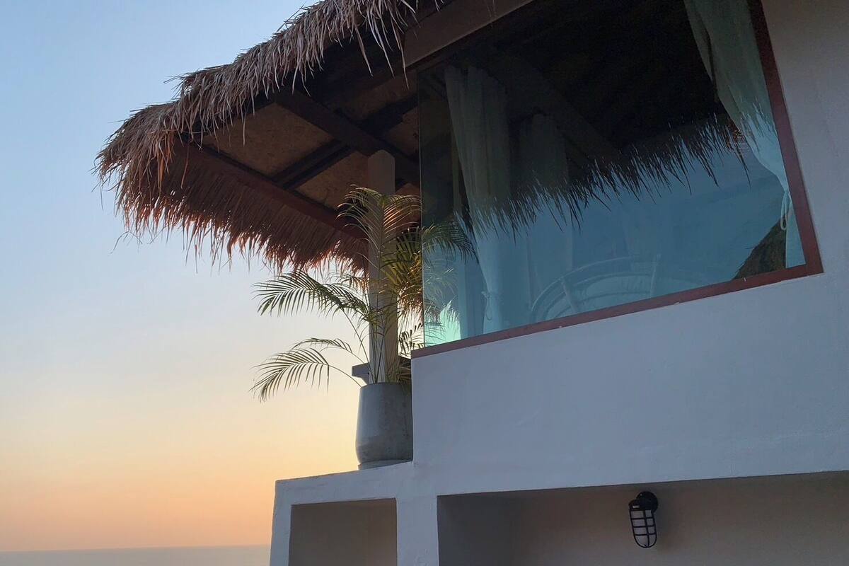 A modern building with a thatched roof and a large window overlooking the sea.