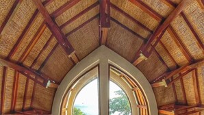 Ein geräumiges Zimmer mit großem Bogenfenster, Holzboden, einem Bett, einem Schreibtisch und Blick ins Grüne.