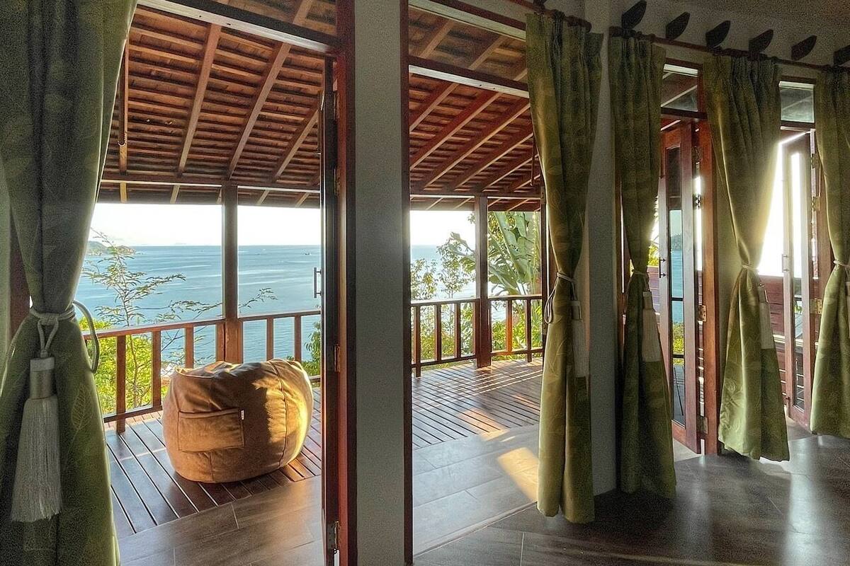 A room with a view of the ocean, a wooden deck, and a large bean bag chair.