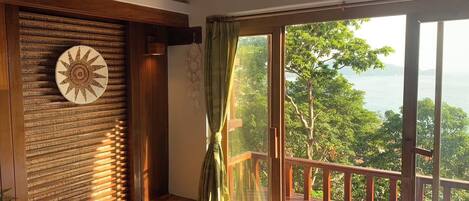 Una habitación con cama, una banca, una pared con diseño circular y vista a un balcón con barandilla.