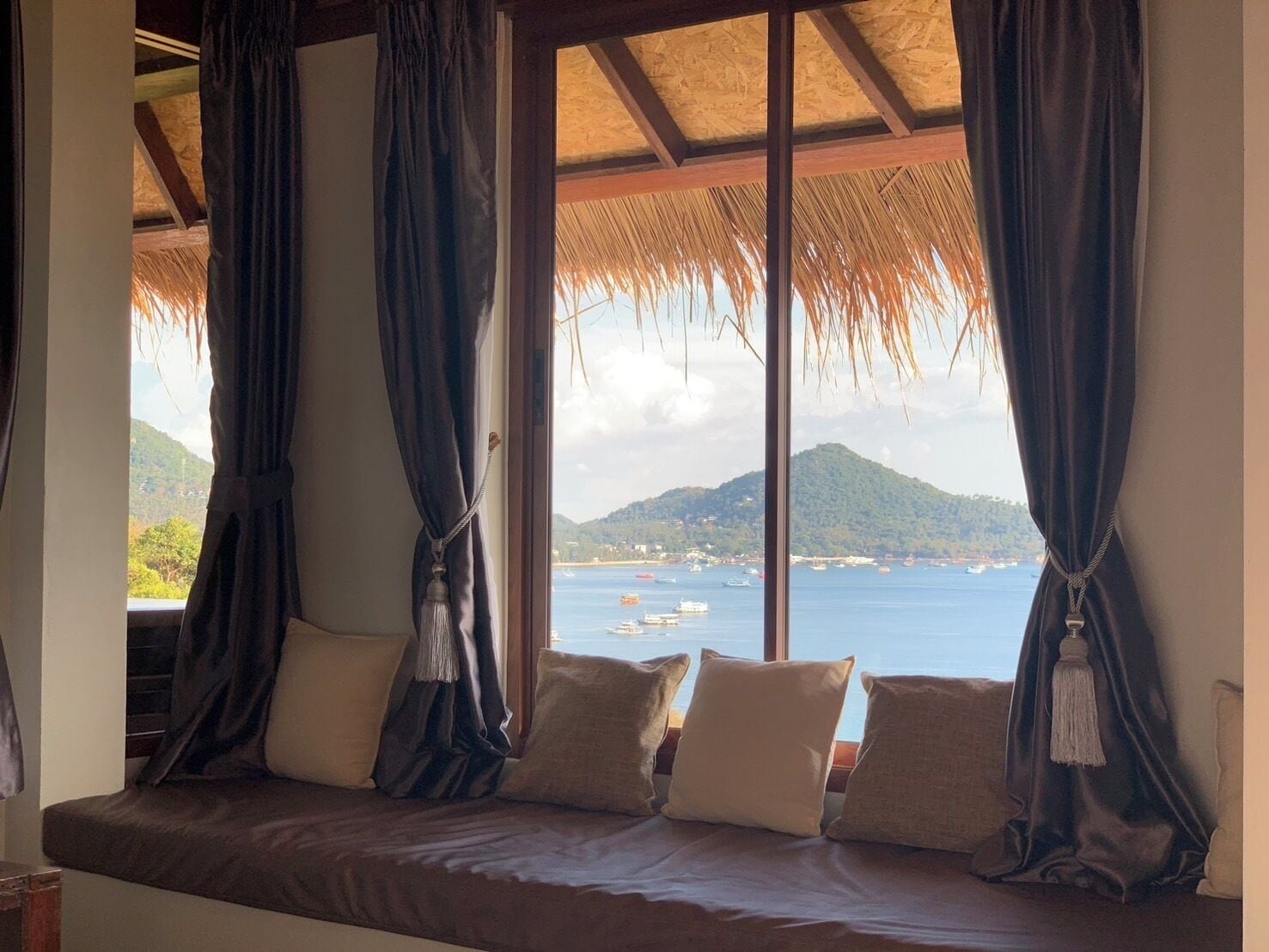 A room with a bed, dark curtains, and a view of the sea and mountains.