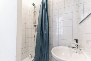 A bathroom with white tiled walls, a shower with a blue curtain, a white sink with a chrome faucet, and a soap dispenser. - Charming 1BR Apt 15 Min to Vienna (Vienna)