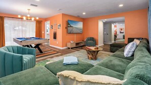 A living room with a pool table, green sofas, and a painting on the wall. - Mins to beach, heated pool, minigolf, fire pit, arcade, dog friendly (Largo)