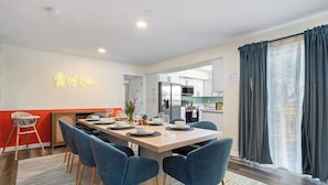 A modern dining area with a long table, blue chairs, and a neon sign on the wall. - Mins to beach, heated pool, minigolf, fire pit, arcade, dog friendly (Largo)