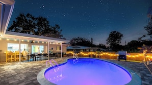 A swimming pool with a built-in slide, surrounded by a patio area with outdoor seating and string lights. - Mins to beach, heated pool, minigolf, fire pit, arcade, dog friendly (Largo)