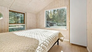 Ein Schlafzimmer mit einem großen Bett, Holzwänden und zwei Fenstern mit Blick auf ein bewaldetes Gebiet.