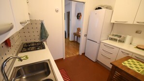 Cocina compacta con estufa a gas, pileta doble y alacenas blancas.